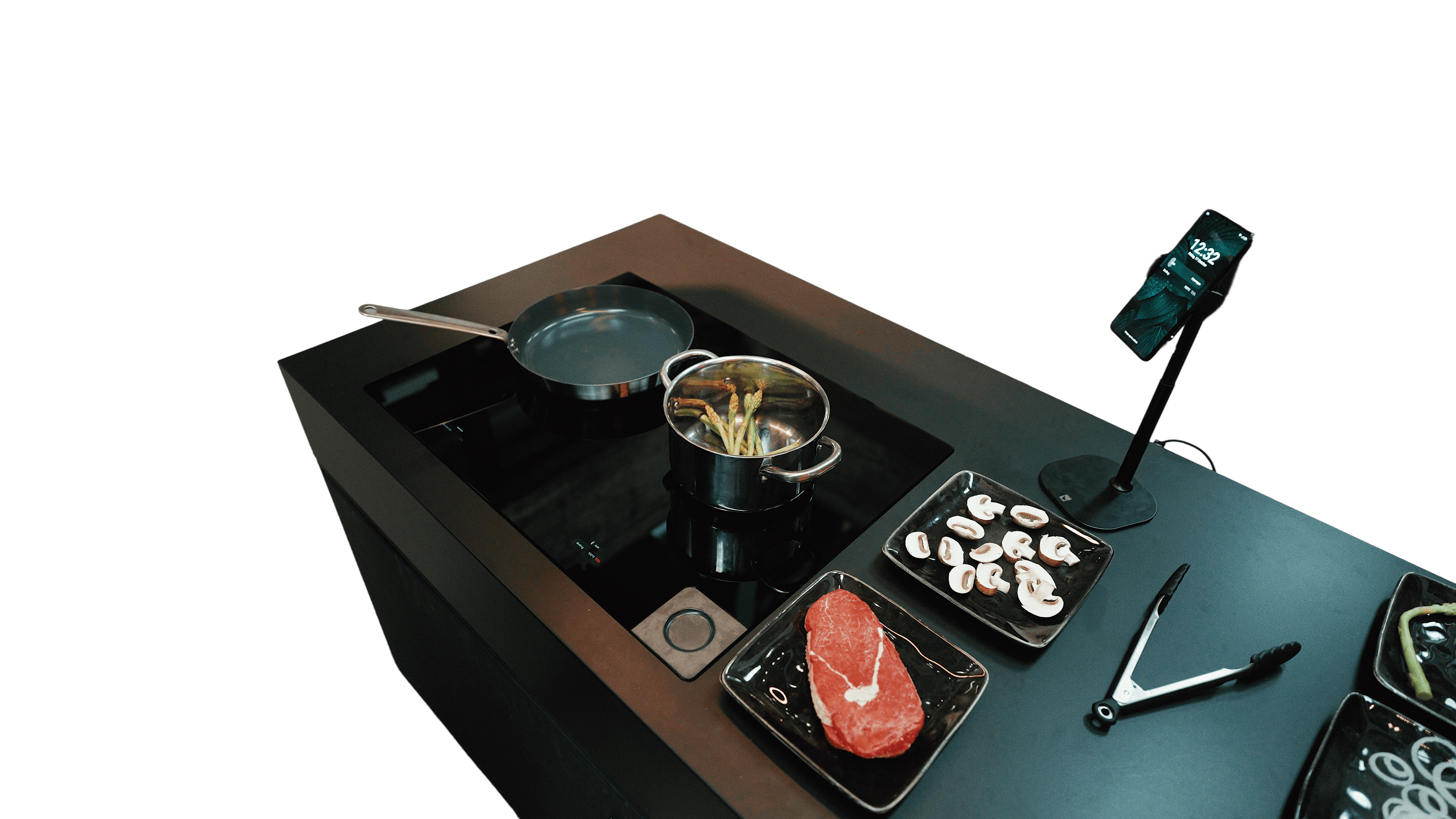 AI kitchen hob demonstration with cookware, ingredients, and a companion phone on a stand